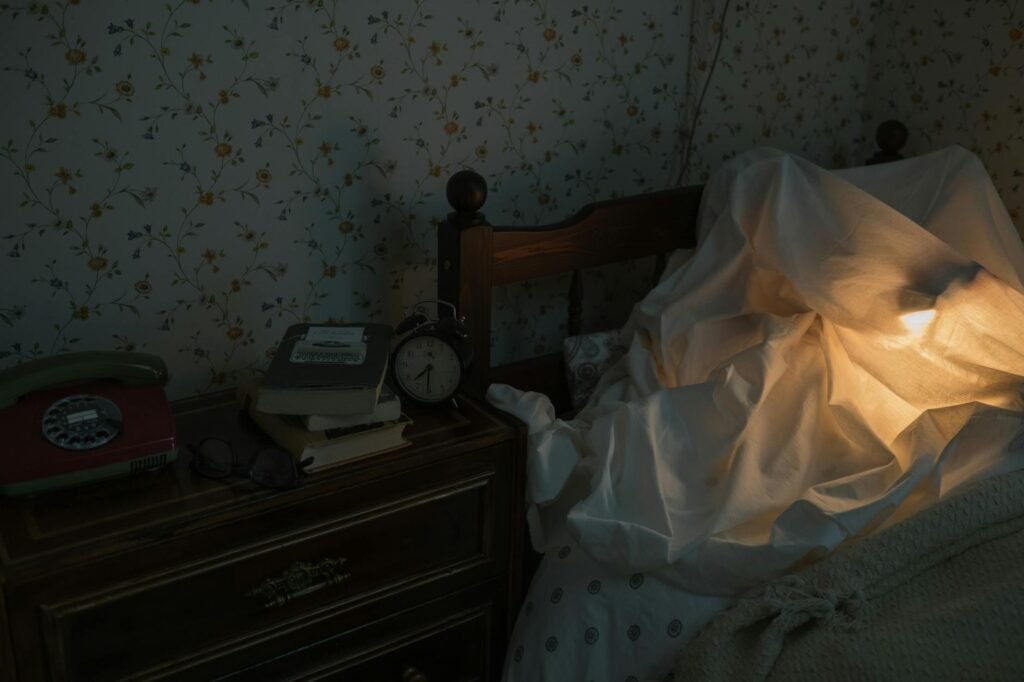 A bedside table with a book, notepad, small lamp, and a phone placed facedown