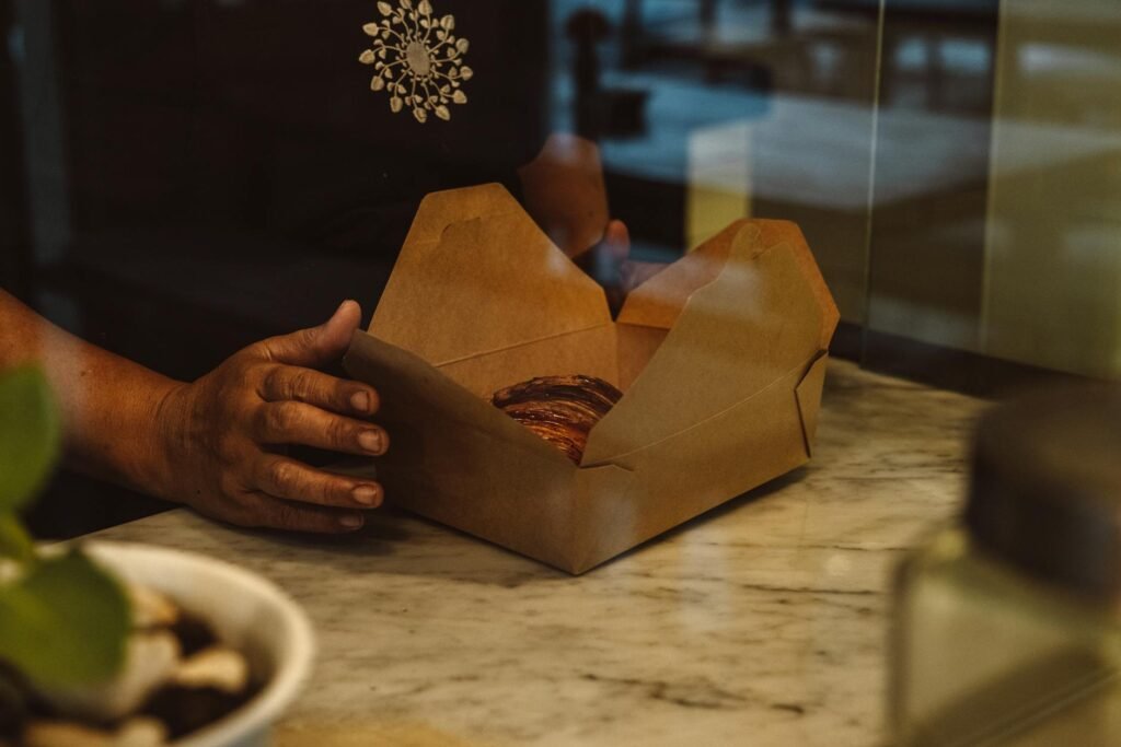 A coffee mug, wine glass, and takeout container on a kitchen counter in the evening.
