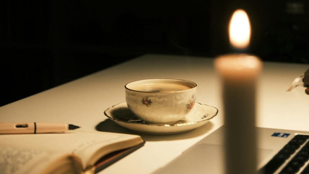A mug of herbal tea beside a closed laptop and notebook on a kitchen counter at night