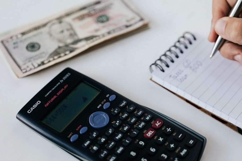 A calculator, notebook, and small household purchases laid out on a desk for a bedroom upgrade budget