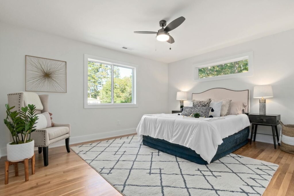 A home thermostat near a bedroom hallway with neatly made bedding and a fan