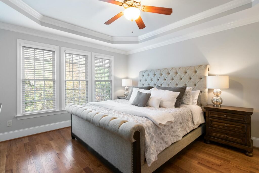A simple box fan next to a bed in a clean, realistic bedroom
