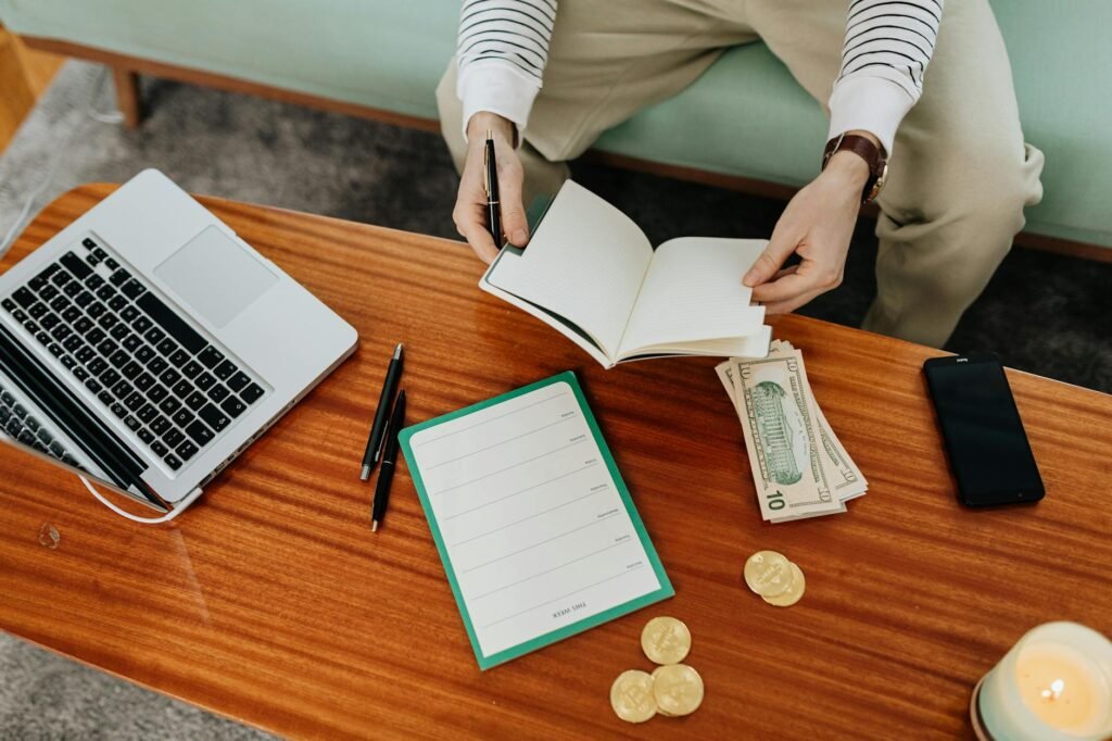 A notebook beside household bills and a pen on a softly lit desk at night
