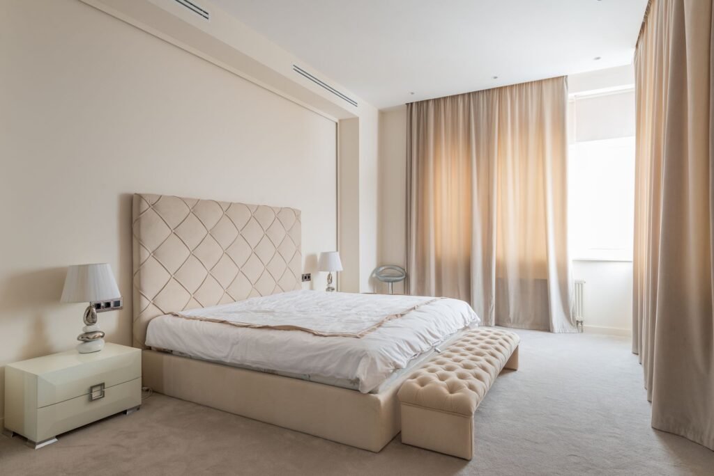 A tidy bedroom with blackout curtains, a small fan, and an uncluttered nightstand