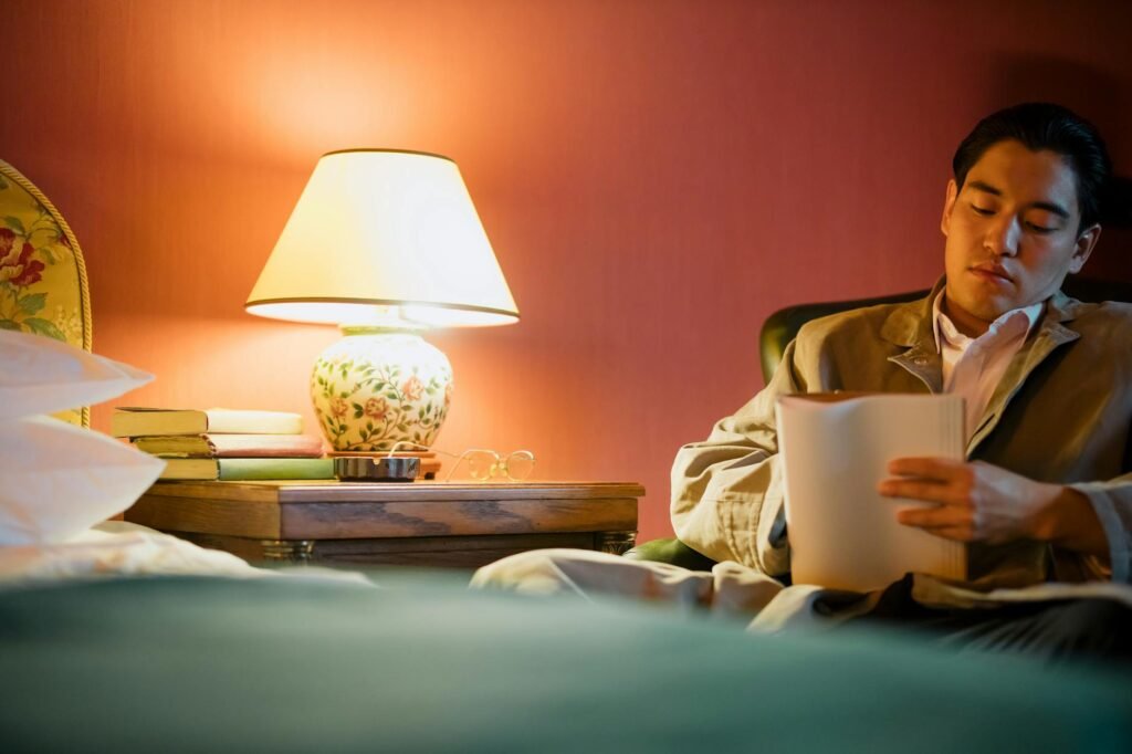 A bedroom nightstand with a book and glasses while a phone charges away from the bed