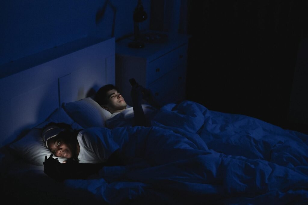 A phone charging on a dresser away from the bed in a dim bedroom