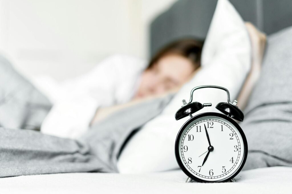 A handwritten sleep log on a notebook next to a basic alarm clock and pen.