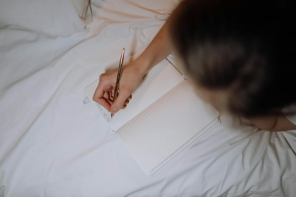 A person writing a short next-day list in a notebook under soft evening light.