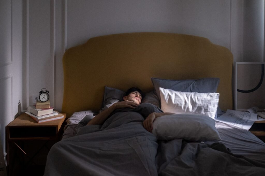 A dark bedroom nightstand with an analog alarm clock, sleep mask, and no glowing screens