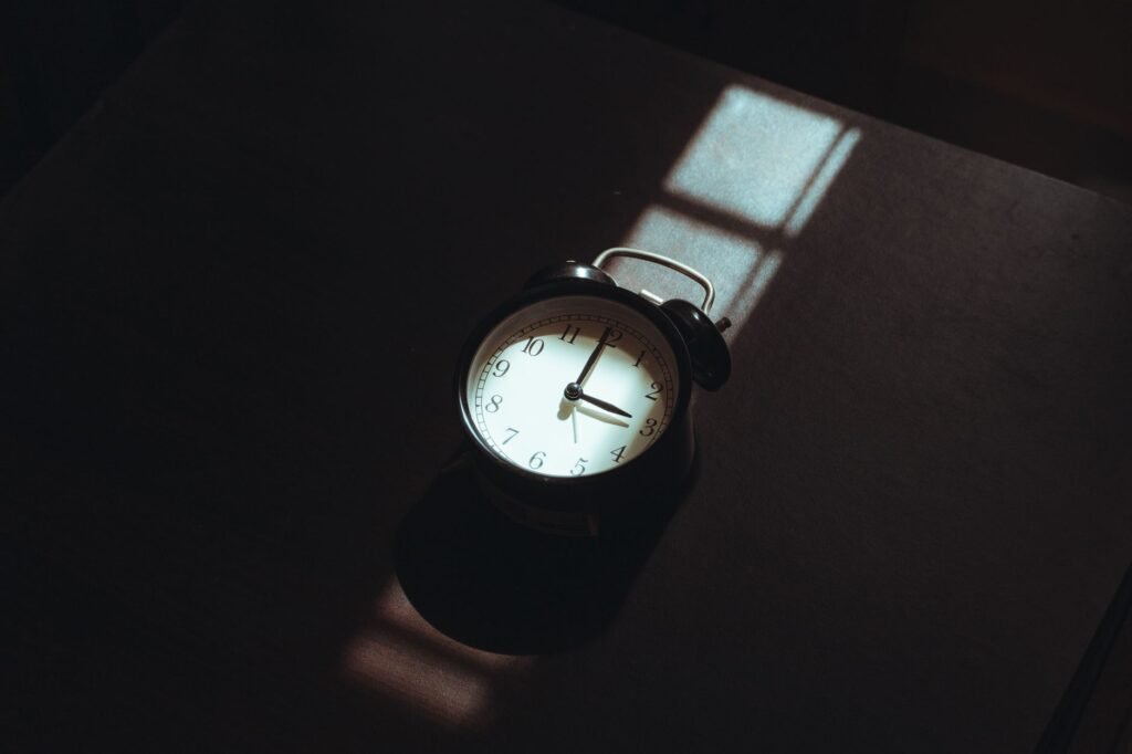 An alarm clock and notebook on a bedside table with natural morning light.