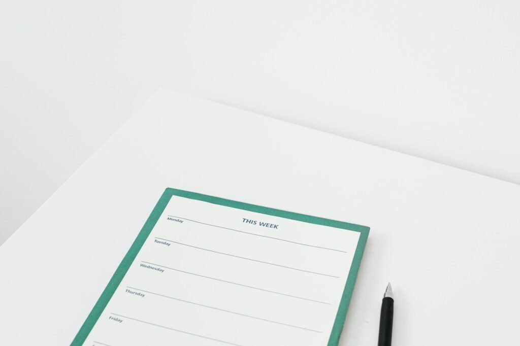 A weekly planner with handwritten bedtime and wake-time notes next to an alarm clock on a desk.
