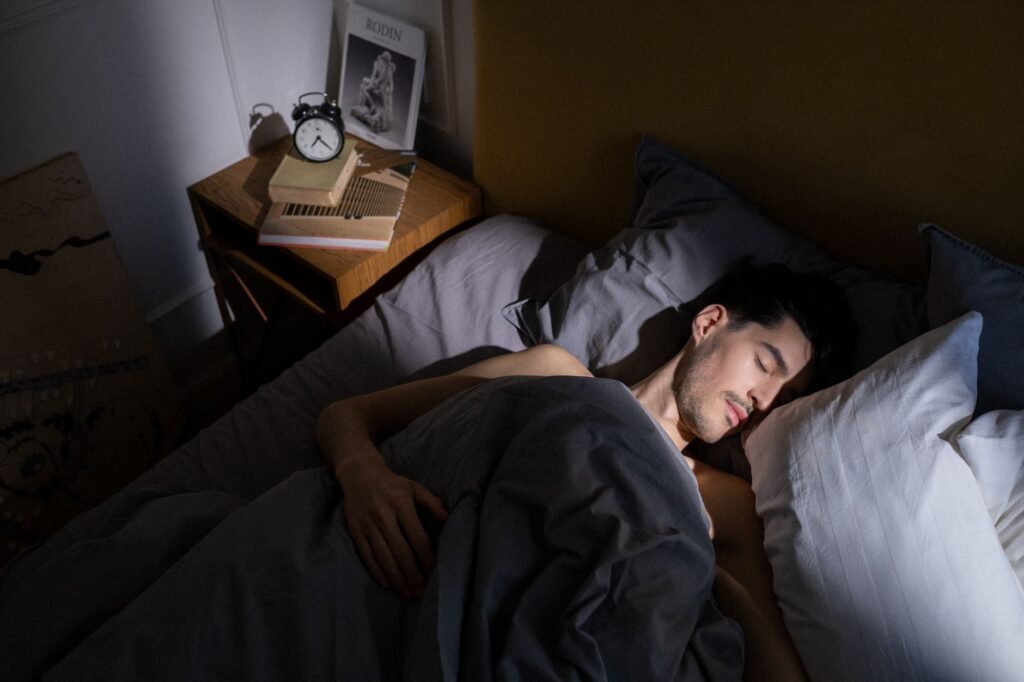 A notebook sleep diary beside an alarm clock and pen on a bedside table